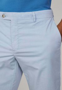 Pantalon en coton bleu clair avec une texture lisse, doté d'une fermeture à bouton, d'une poche avant et d'une coupe ajustée. Design simple, sans motifs.