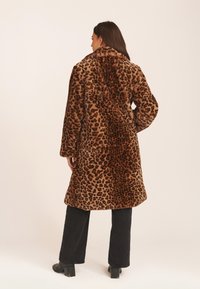 Leopard print faux fur coat with a relaxed silhouette, side pockets, and a collar, paired with black wide-leg pants and ankle boots.