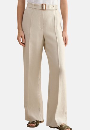 Beige High-Waist-Hose mit weitem Bein, vorderen Bügelfalten und passendem Gürtel mit rechteckiger Schnalle, getragen zu braunen Sandalen mit Nieten.