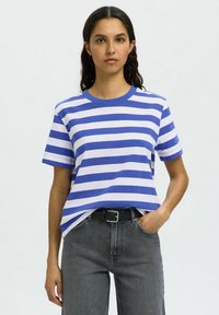 Mėlynos ir baltos dryžuotos t-shirts su apykakle, trumpomis rankovėmis ir laisvu siluetu. Stiliuojama su aukšto liemens pilkais džinsais ir juodu diržu.