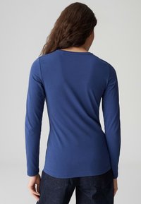 Marineblaues Langarmshirt aus weichem Stoff, mit rundem Halsausschnitt und taillierter Passform. Nahtdetails sind an den Schultern sichtbar.