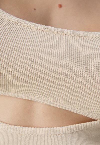 Beige cropped top featuring ribbed texture, wide neckline, and cut-out detail along the side, highlighting smooth fabric and stretch.
