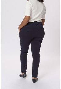 Sorte, tætsiddende bukser med en strækbar talje, to baglommer og opsmøg ved anklerne, parret med en kortærmet, cremefarvet top.