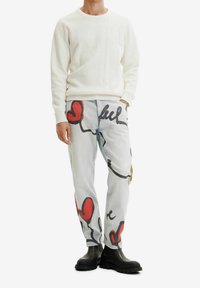 Suéter blanco texturizado con cuello redondo, combinado con pantalones azul claro que presentan diseños abstractos coloridos y botas negras brillantes hasta el tobillo.