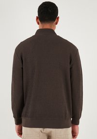 Giacca in corduroy marrone con colletto alto, texture a righe e maniche lunghe. Caratterizzata da una fascia in vita scura e dettagli sui polsini.