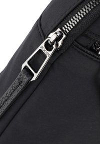 Borsa nera in nylon con una cerniera argentata e un tirante in pelle nera a trama, che presenta un design elegante e un'estetica minimalista.