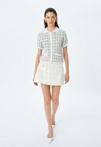 Tweed top met korte mouwen, kraag en knoopsluiting, gecombineerd met een geruite mini-rok met twee voorzakken en parelaccenten.
