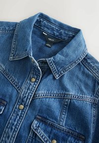 Jeansjacka i medelblått med spetsig krage, knappknäppning i guldton, två framfickor och kontrasterande sömmar.