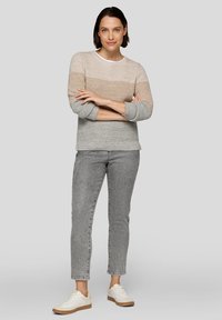 Helles Sweatshirt mit beigen und grauen horizontalen Streifen, Rundhalsausschnitt und gerippten Bündchen. Kombiniert mit grauen Jeans und weißen Sneakers.