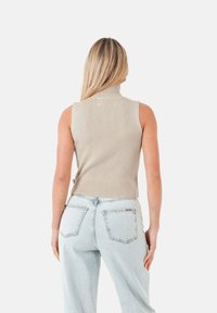 Top senza maniche a collo alto a coste beige abbinato a jeans in denim chiaro a vita alta. Dettagli visibili delle tasche posteriori sui jeans.