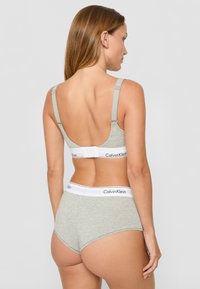 Šviesiai pilkas medvilninis liemenėlės ir aukštai juosmeninės kelnaitės komplektas su elastine juosta, kuriame pavaizduotas "Calvin Klein" logotipas. Lygus paviršius ir paprastas dizainas.