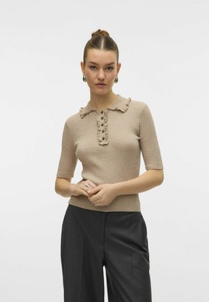 Maglione polo beige a costine con colletto arricciato, maniche corte e dettagli in bottone lungo la parte anteriore. Abbinato a pantaloni scuri.