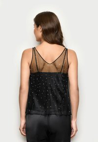 Camisola nera con schiena trasparente, decorata con paillettes argentate. Spalline regolabili, scollatura a V, tessuto morbido con un design fluido.