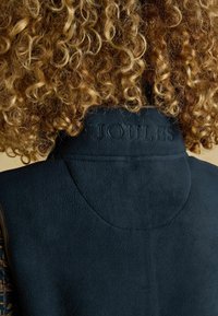 Sötétkék polármellény, puha tapintással és a nyakon elhelyezett, gravírozott "JOULES" logóval. Kerek nyakkivágással és sima felülettel rendelkezik.