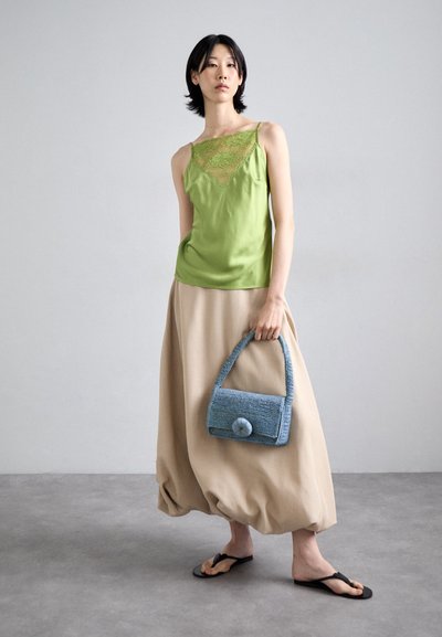 Satin green camisole with lace detailing paired with a beige, voluminous skirt. Carrying a blue woven handbag with a prominent button. Black flip-flops.