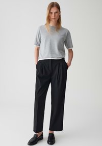 Grijze korte mouw trui met een ronde hals, gecombineerd met hoge zwarte geplooide broek. Zwarte instaplaarzen maken de look compleet.