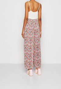 Jumpsuit floral avec un haut blanc, motif de fleurs multicolores, taille élastique et design à jambes larges, associé à des chaussures à talons blocs roses clairs.