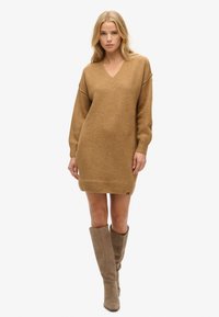 Vestido de mangas largas y escote en V en un cálido color camel texturizado, con un corte holgado que termina justo por encima de la rodilla. Presenta un pequeño detalle de logo.