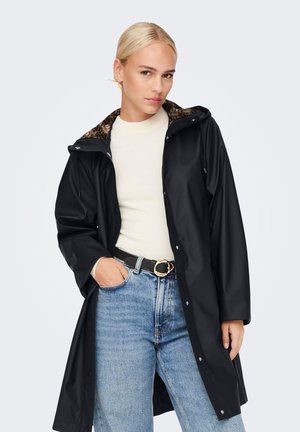 Black waterproof raincoat with a hood, featuring a leopard print lining and snap closure. Paired with a cream top and high-waisted jeans.