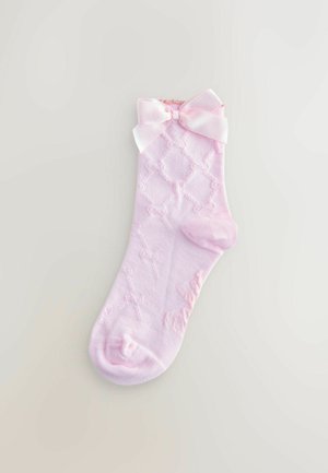 Roosa puuvillane sokk, millel on rubiinimuster, pehme tekstuur ja dekoratiivne satiinist lips varruka ääres. Tallaosas on õrn bränding.