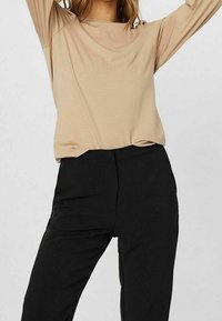 Beige Langarmoberteil mit lockerer Passform und Rundhalsausschnitt, kombiniert mit schwarzen Slim-Fit-Hosen, glattem Stoff und ohne sichtbare Muster.