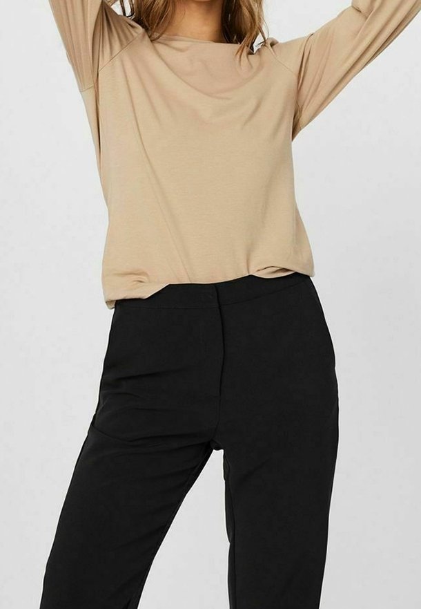 Beige Langarmoberteil mit lockerer Passform und Rundhalsausschnitt, kombiniert mit schwarzen Slim-Fit-Hosen, glattem Stoff und ohne sichtbare Muster.