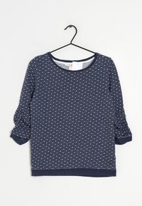Camisa de manga larga azul marino con puntos blancos, textura acanalada, cuello redondo y mangas fruncidas. Etiqueta adjunta cerca del cuello.