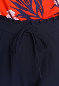 Námořnické modré kalhoty s jemnou texturou, s elastickým pasem na šňůrku a sklady, spárované s jasně červeným květinovým topem.