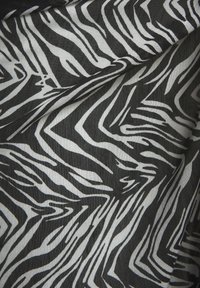 Schwarz-weißer, zebramustered Stoff mit Falten und sichtbarer Textur, der ein unregelmäßiges Tierdruckmuster zeigt.