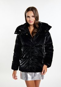 Giacca puffa nera realizzata in materiale lucido, con colletto alto, tasche frontali e chiusura con zip. Abbinata a una gonna argentata lucida.