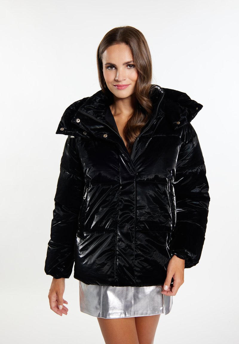 Giacca puffa nera realizzata in materiale lucido, con colletto alto, tasche frontali e chiusura con zip. Abbinata a una gonna argentata lucida.