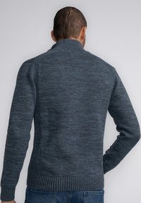 Suéter de punto azul oscuro con cuello alto, puños y dobladillo acanalados, que presenta un patrón texturizado y una silueta ajustada.
