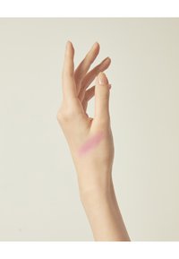 Main dans une texture lisse, montrant un échantillon de blush rose pâle sur la paume. Les ongles sont coupés et naturels. L'arrière-plan est neutre.