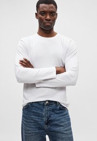 Hvit langermet T-skjorte laget av glatt bomull, kombinert med midtblå denimjeans med klassisk passform og subtil fading.