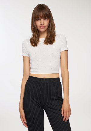 T-shirt bianco corto con maniche corte, decorato con strass argentati. Abbinato a pantaloni neri a righe sottili a vita alta.