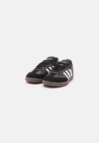 Baskets de sport noires avec des rayures blanches, tige en suède et synthétique, semelle en caoutchouc et design bas classique.