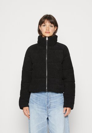 Doudoune noire avec col montant, fermeture éclair et design matelassé. Fabriquée en tissu texturé, associée à un jean loose bleu clair.