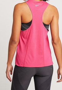 Rosa sportlinne med racerback-design och meshstruktur. Används över en svart sport-bh med ränder och tights för träning.