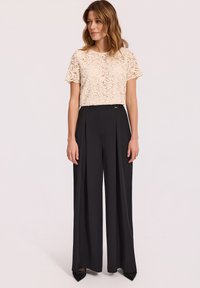 Koronkowa bluzka w kremowym kolorze z okrągłym dekoltem i krótkimi rękawami, połączona z czarnymi spodniami o szerokich nogawkach z wysokim stanem i plisami.
