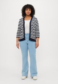 Striped cardigan in navy and white, buttoned front, ribbed cuffs, paired with light blue flared jeans and white sneakers.