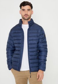 Giacca puffer blu navy con design trapuntato, colletto alto, zip frontale e tasche laterali. Il tessuto ha una texture liscia e lucida.