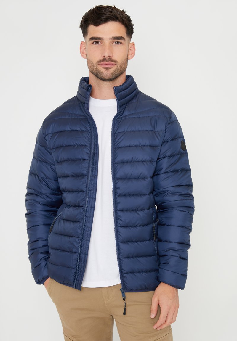 Giacca puffer blu navy con design trapuntato, colletto alto, zip frontale e tasche laterali. Il tessuto ha una texture liscia e lucida.