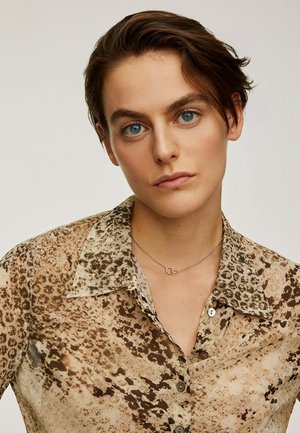Camisa translúcida de leopardo en tonos marrones y beige, con cuello, parte delantera abotonada y un delicado collar de plata con un pendiente circular.