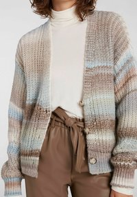 Sweter robiony na drutach w jasnobrązowe, niebieskie i kremowe paski. Posiada luźny krój, teksturowany wzór oraz dwa guziki z przodu.