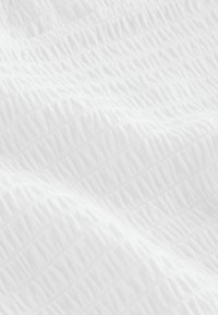 Gros plan d'un tissu blanc doux à texture avec un motif matelassé subtil créant de petites crêtes et ondulations surélevées.