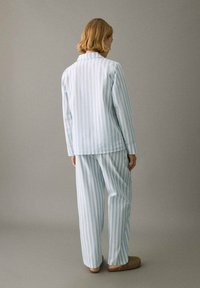 Conjunto de pijama de rayas azules y blancas hecho de tela ligera, que incluye una camisa de manga larga y pantalones holgados. Destaca por su cuello recto.