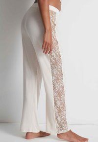 Pantalon de lounge blanc avec un panneau latéral en dentelle transparente, design à jambes droites et texture douce. Taille élastique pour le comfort.