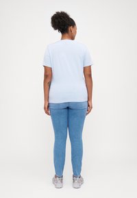 T-shirt bleu clair à manches courtes associé à un jean slim en denim clair. Le mannequin porte des baskets argentées et a une coiffure texturée.