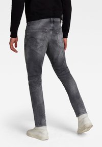 Slim-fit grå denimjeans med lätt urtvättning, femficksdesign och broderade bakfickor, ihopparade med vita sneakers.