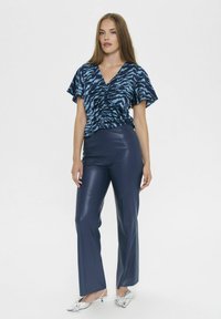 Marineblaues, kurzärmeliges Oberteil mit einem Tigerstreifenmuster und Raffung an der Vorderseite, kombiniert mit dunkelblauen, hochtaillierten, aus Kunstleder gefertigten Hosen.